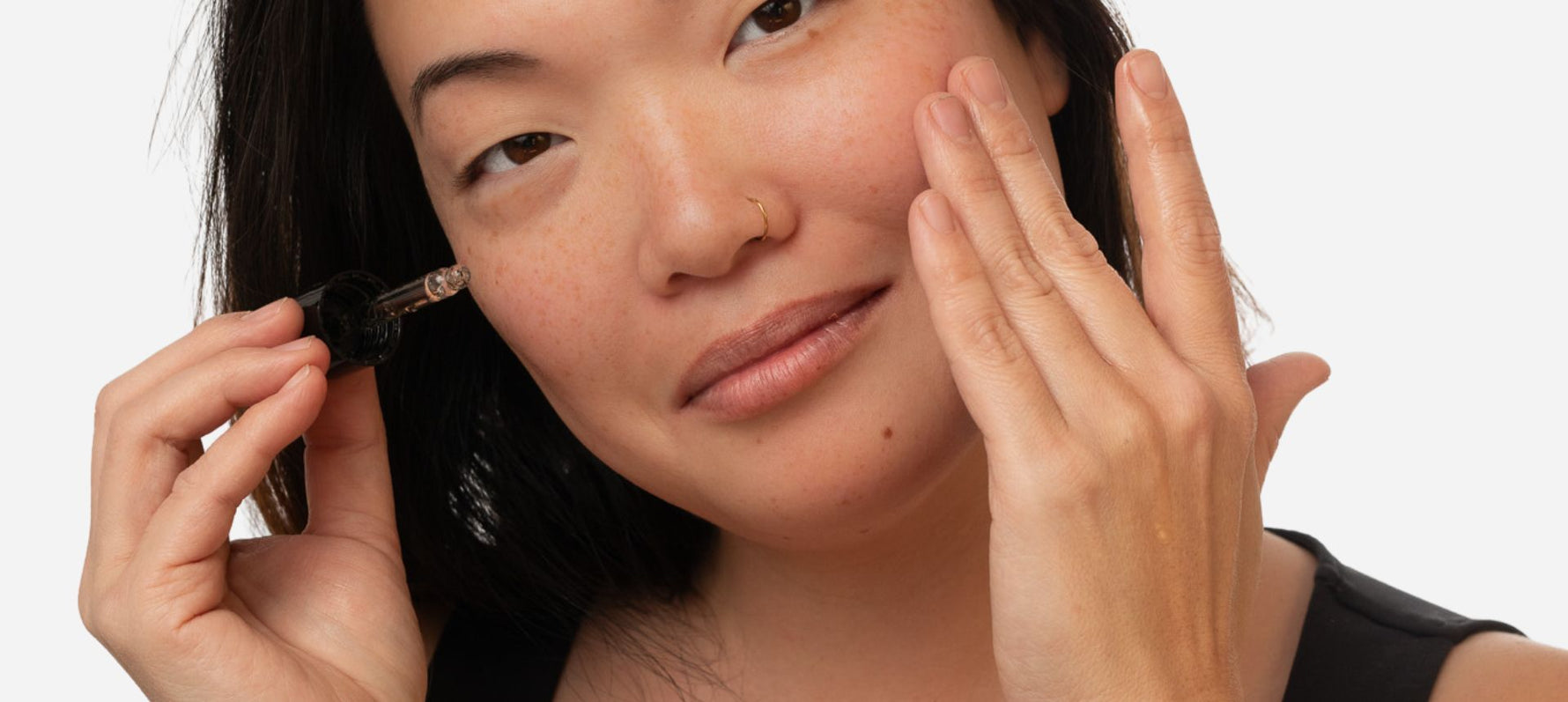natural skincare routine for aging skin. Model with serum dropper next to skin.