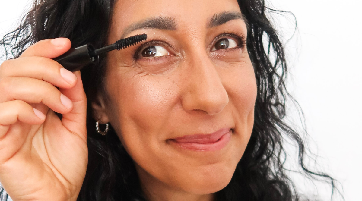 Woman smiling while putting on botanical mascara