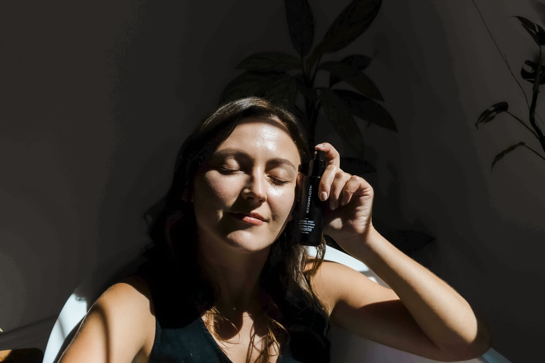 Woman Holding withSimplicity Facial Mist Spray by face with dark background