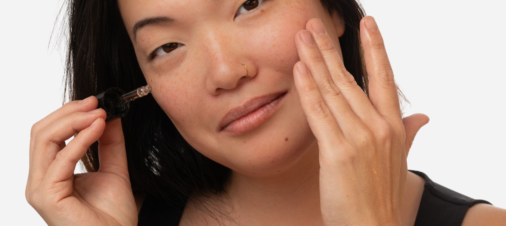 natural skincare routine for aging skin. Model with serum dropper next to skin.