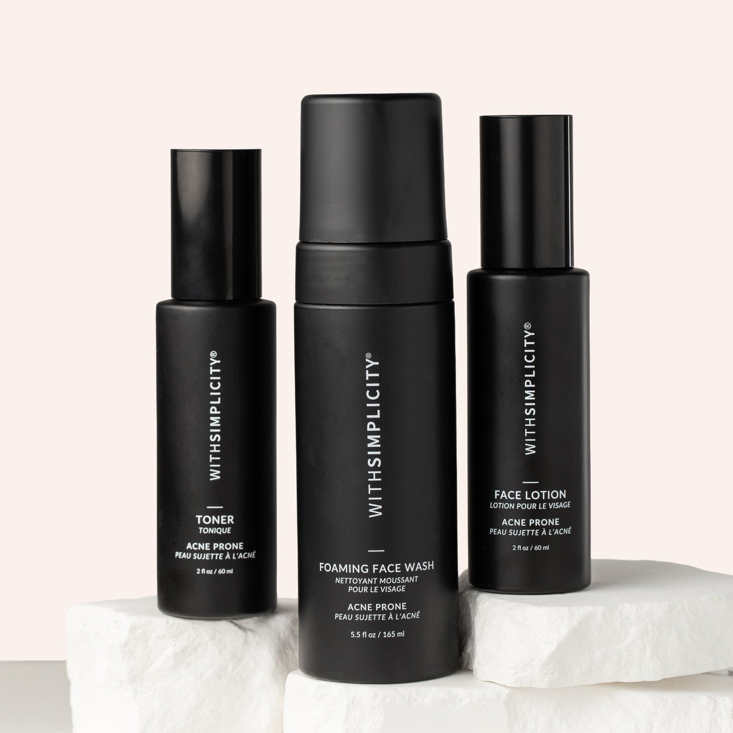 Three withSimplicity acne-prone skincare products—one toner bottle, one lotion bottle, and a foaming face wash—arranged on stone with soft beige background.