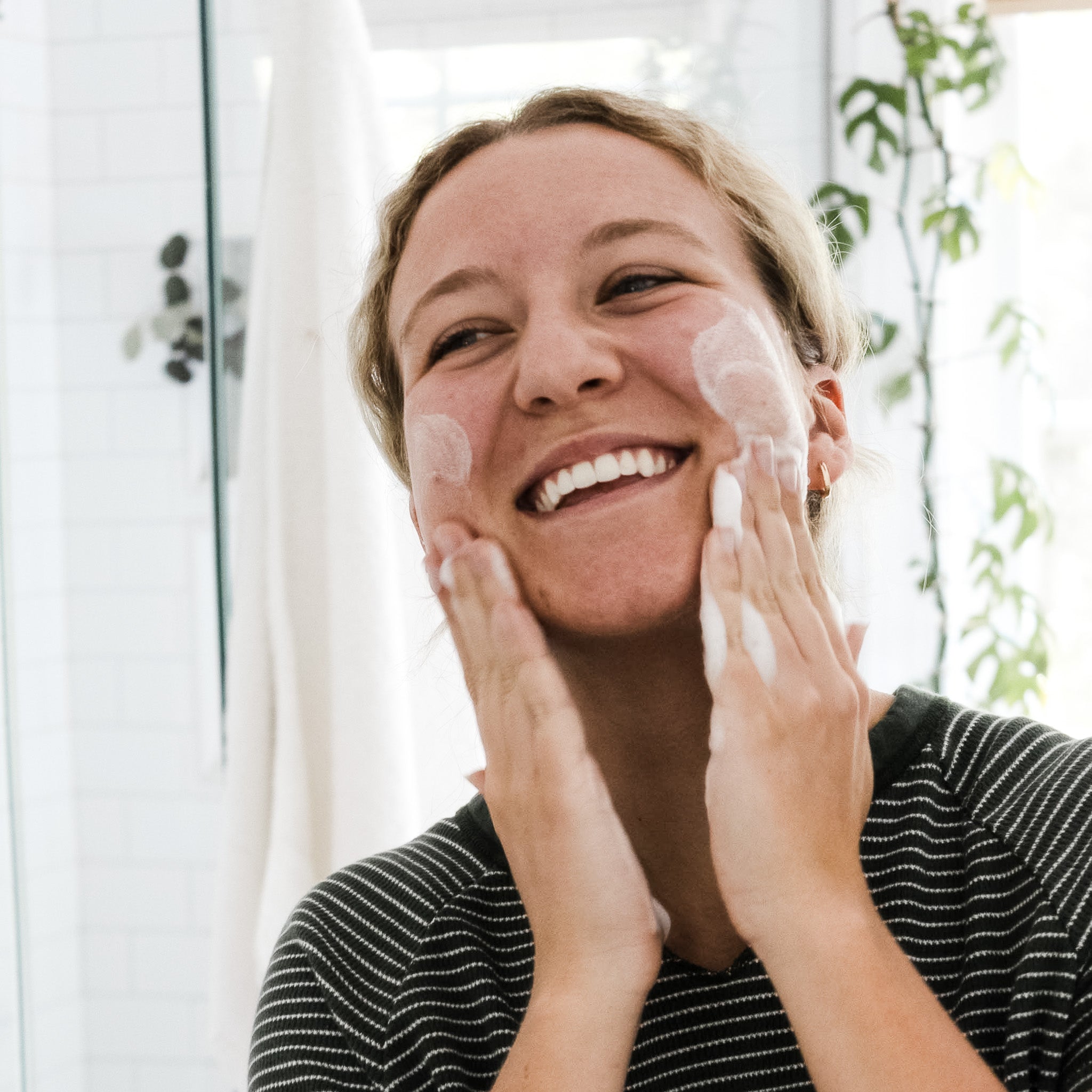 Woman applying cream to her face with a bright background