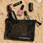 Set of beauty products including bottles and a pouch on sand with shells and starfish.