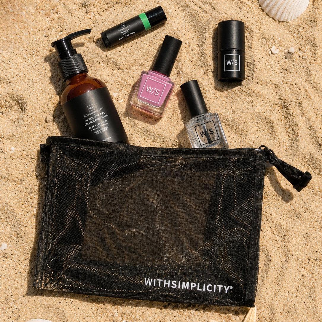 Set of beauty products including bottles and a pouch on sand with shells and starfish.