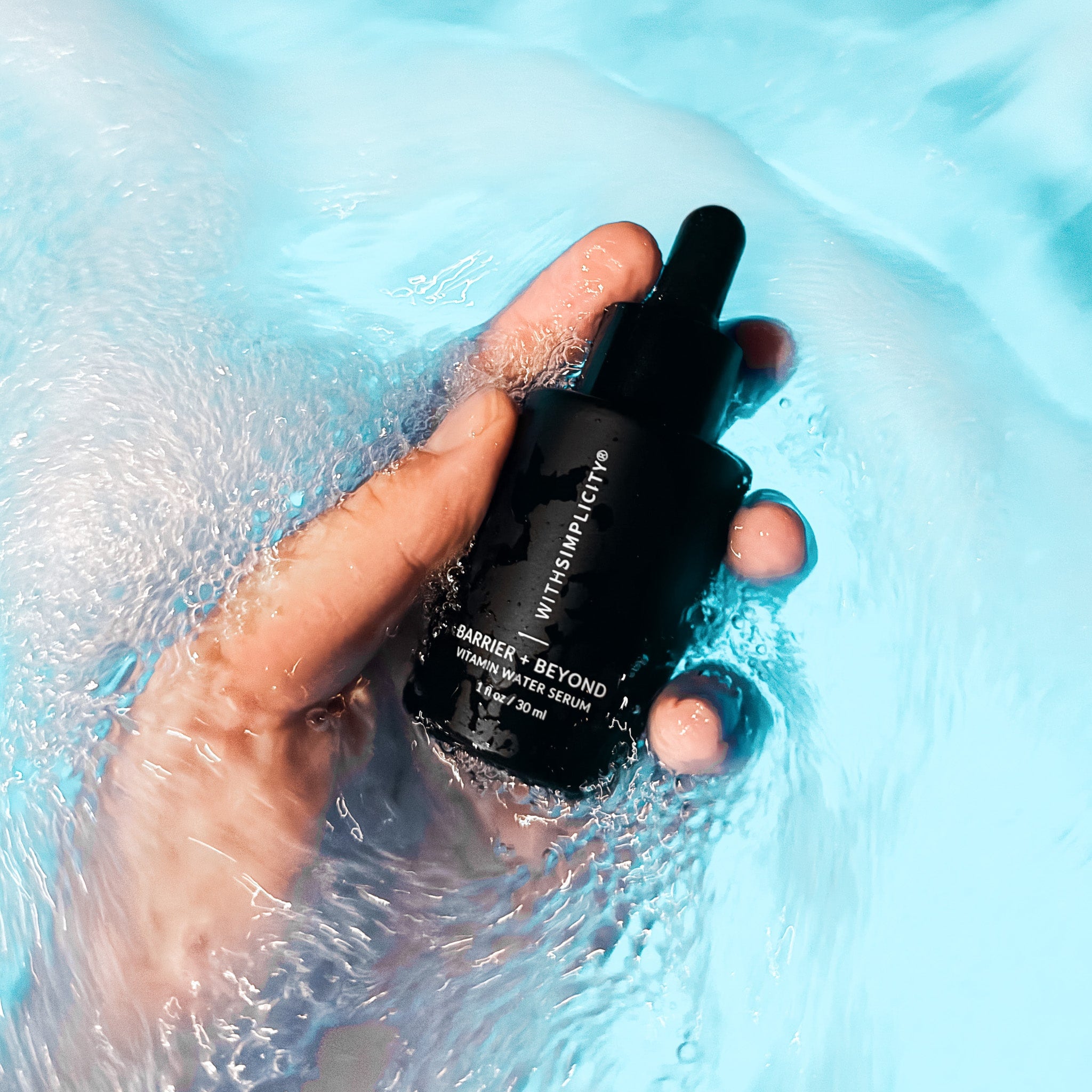Hand holding a black skincare bottle of withSimplicity Barrier & Beyond Vitamin Water Serum in water