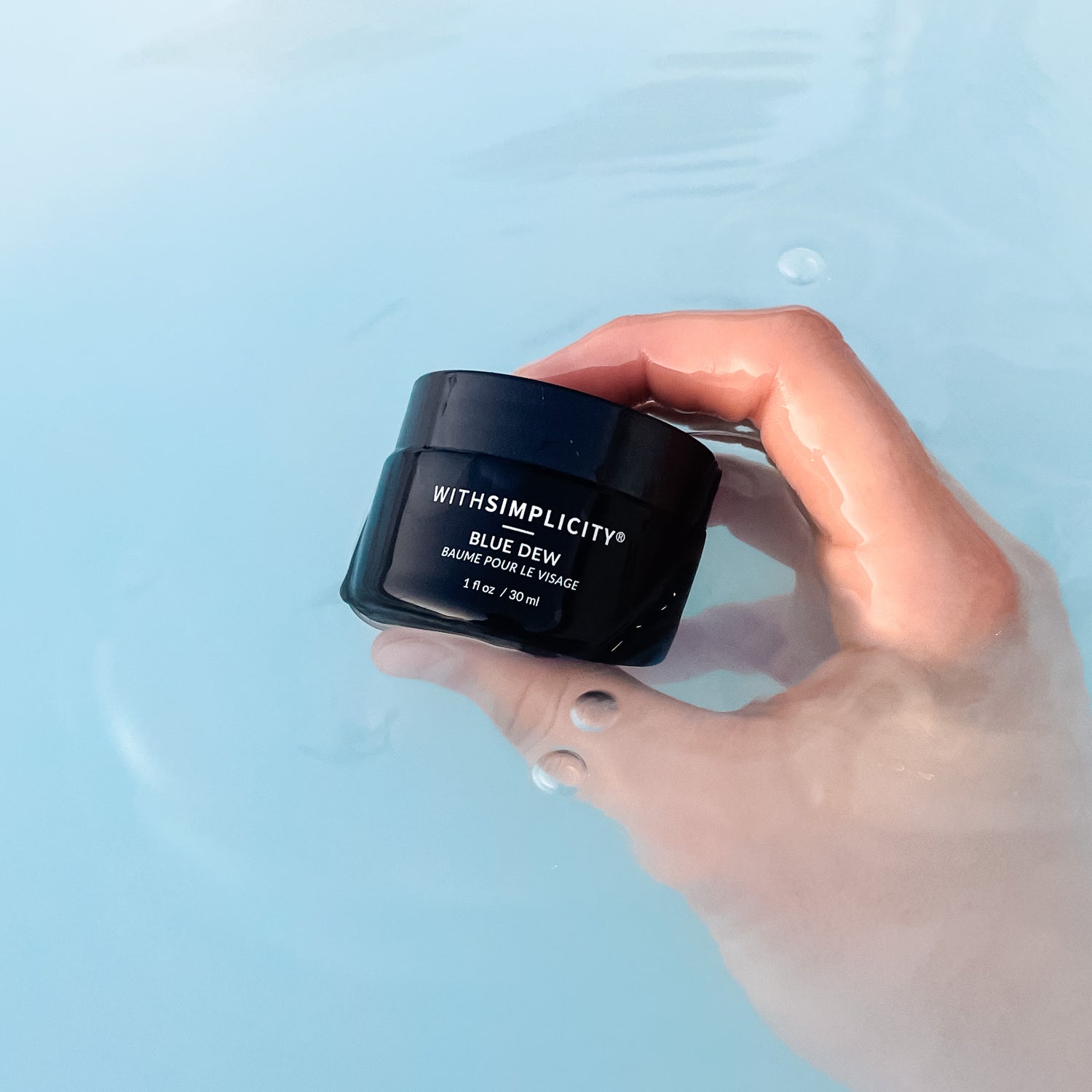 Hand holding withSimplicity Blue Dew moisturizer slightly in a milky blue water.