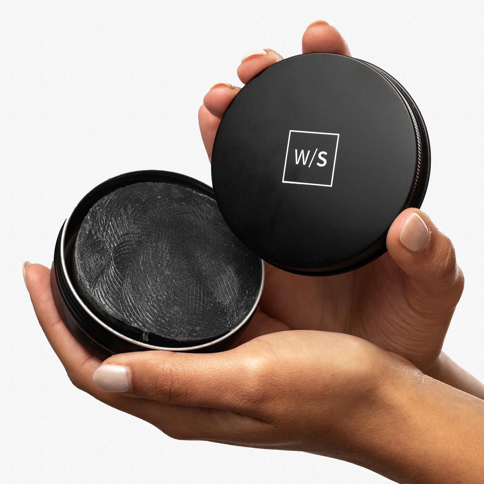 Hand holding withSimplicity Charcoal Face Bar in a black tin with the withSimplicity logo on it.