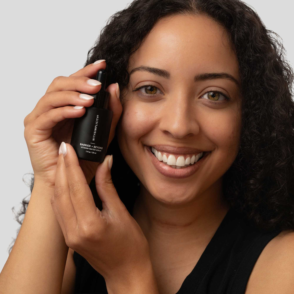 woman holding withSimplicity Barrier and beyond vitamin water serum by face against a light gray background