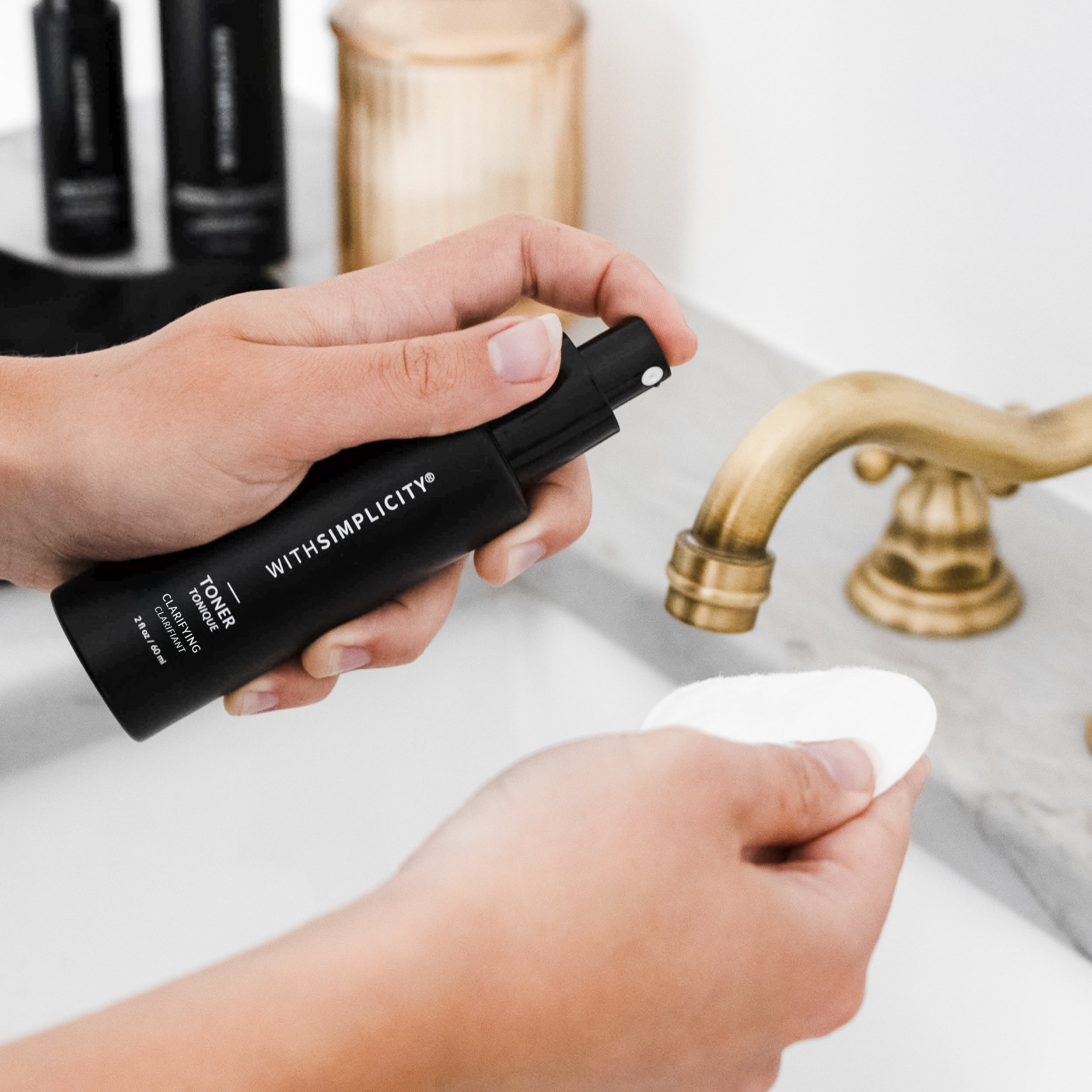Hand holding withSimplicity Clarifying toner over sink and spraying product onto a cotton round