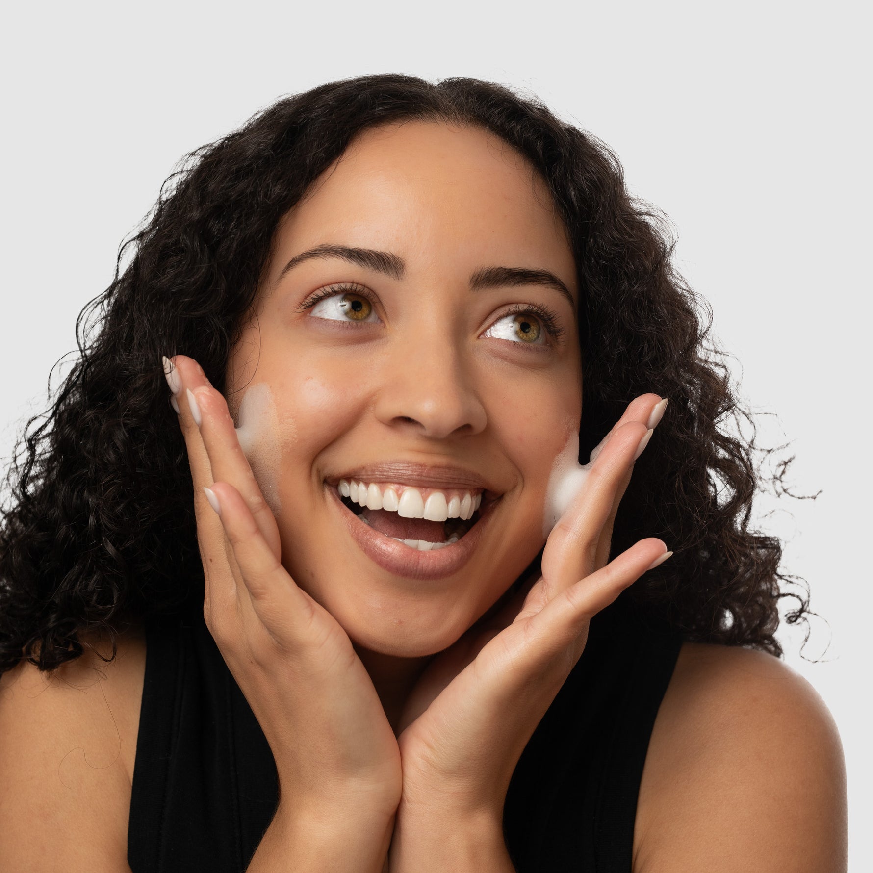 Woman putting foaming face wash on face against a light gray background