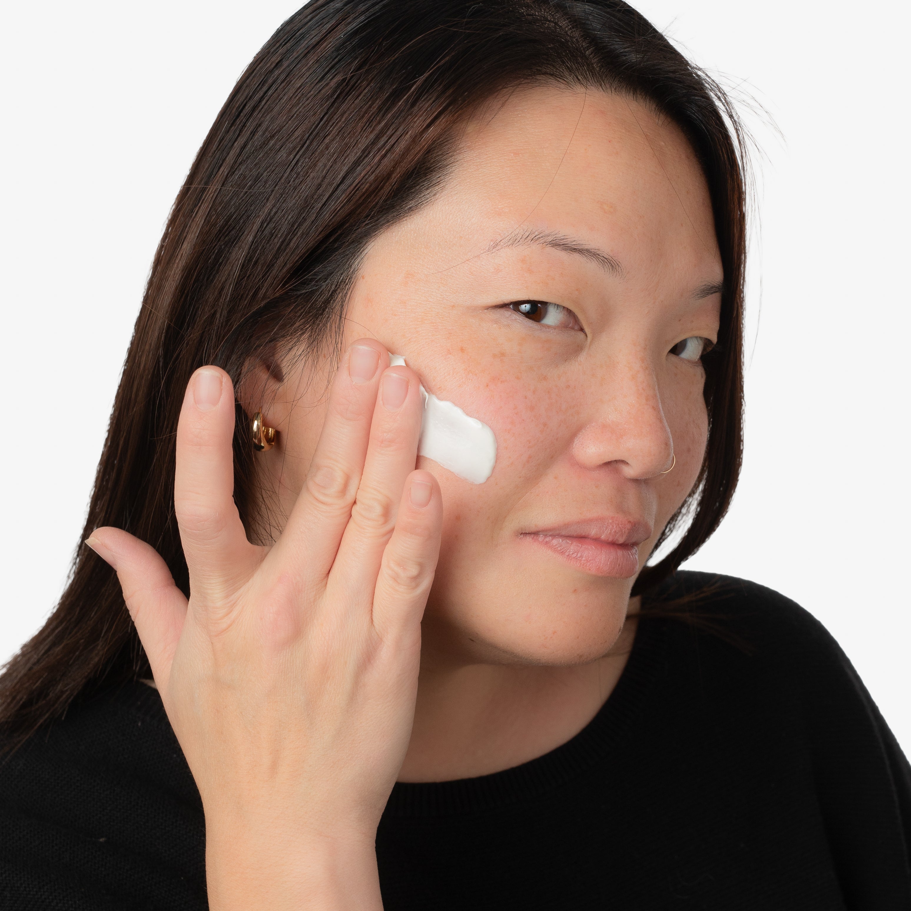 woman with dark hair and black shirt applying withSimplicity Pro-Age Cleanser to face against light gray background