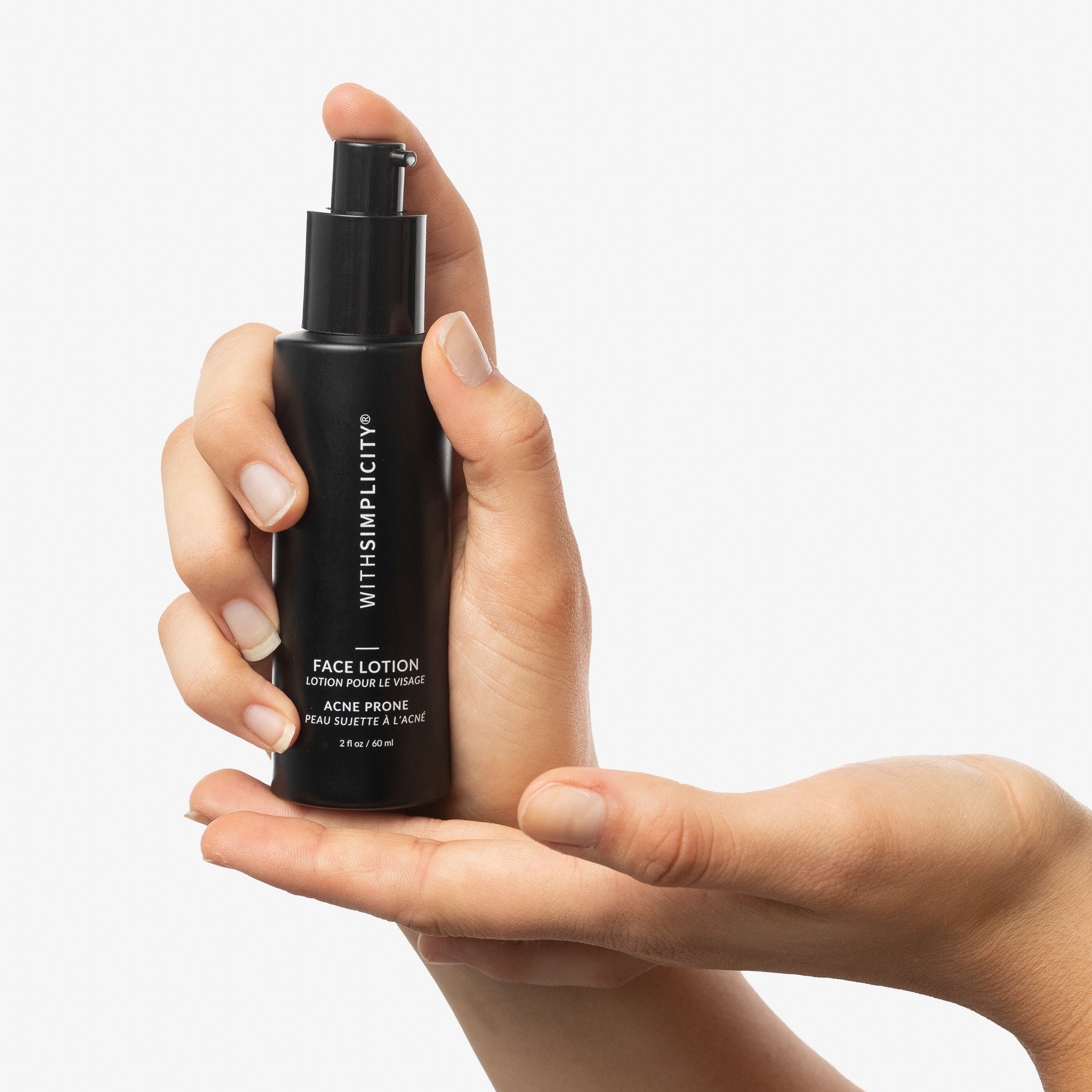 Hand holding a black bottle of withSimplicity Acne Prone Face Lotion against a neutral background