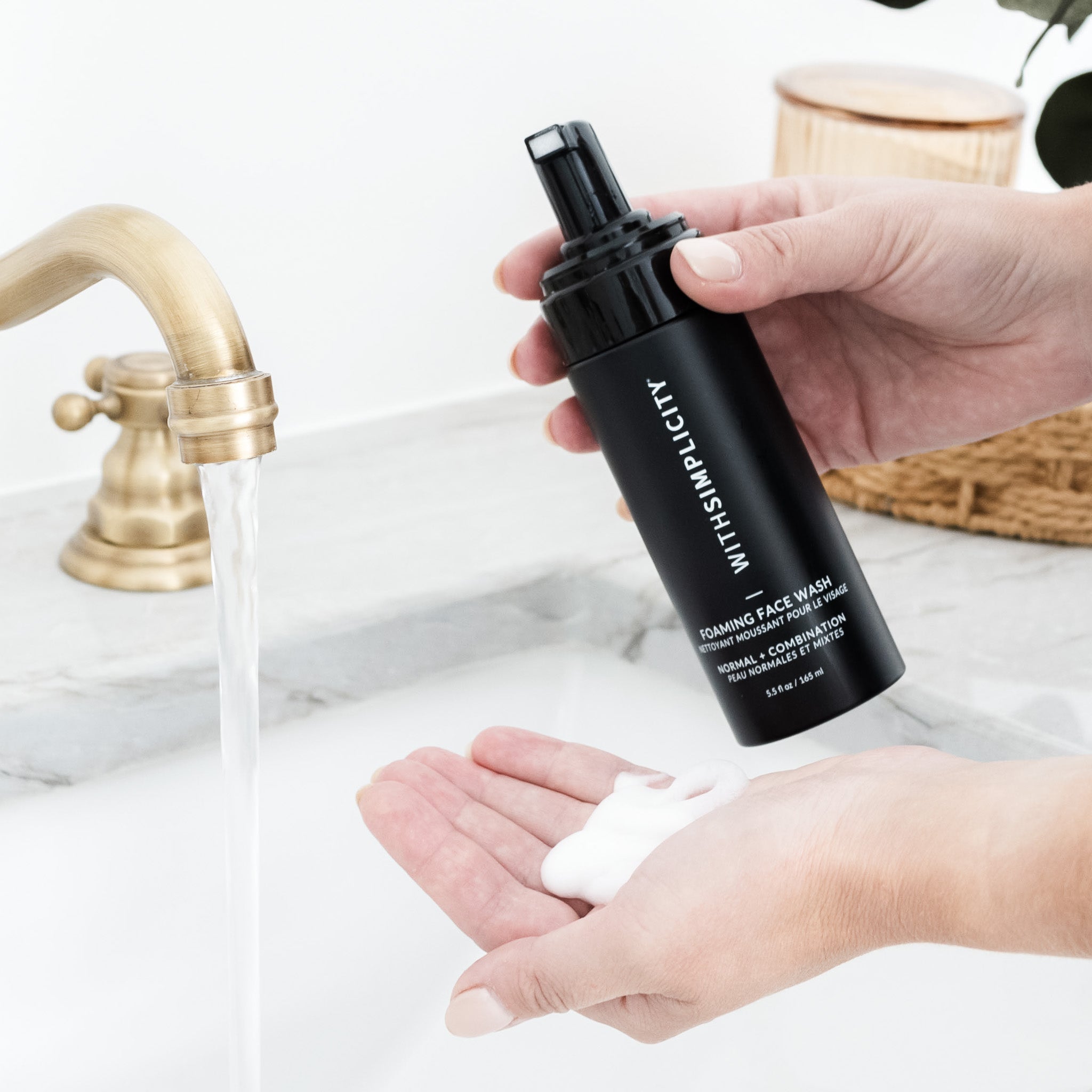 Person holding withSimplicity Foaming Face Wash Normal and Combination Bottle with soap on their hands in a bathroom setting.