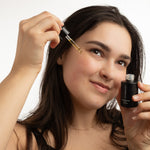 Woman applying a dropper of oil to her hair against a neutral background