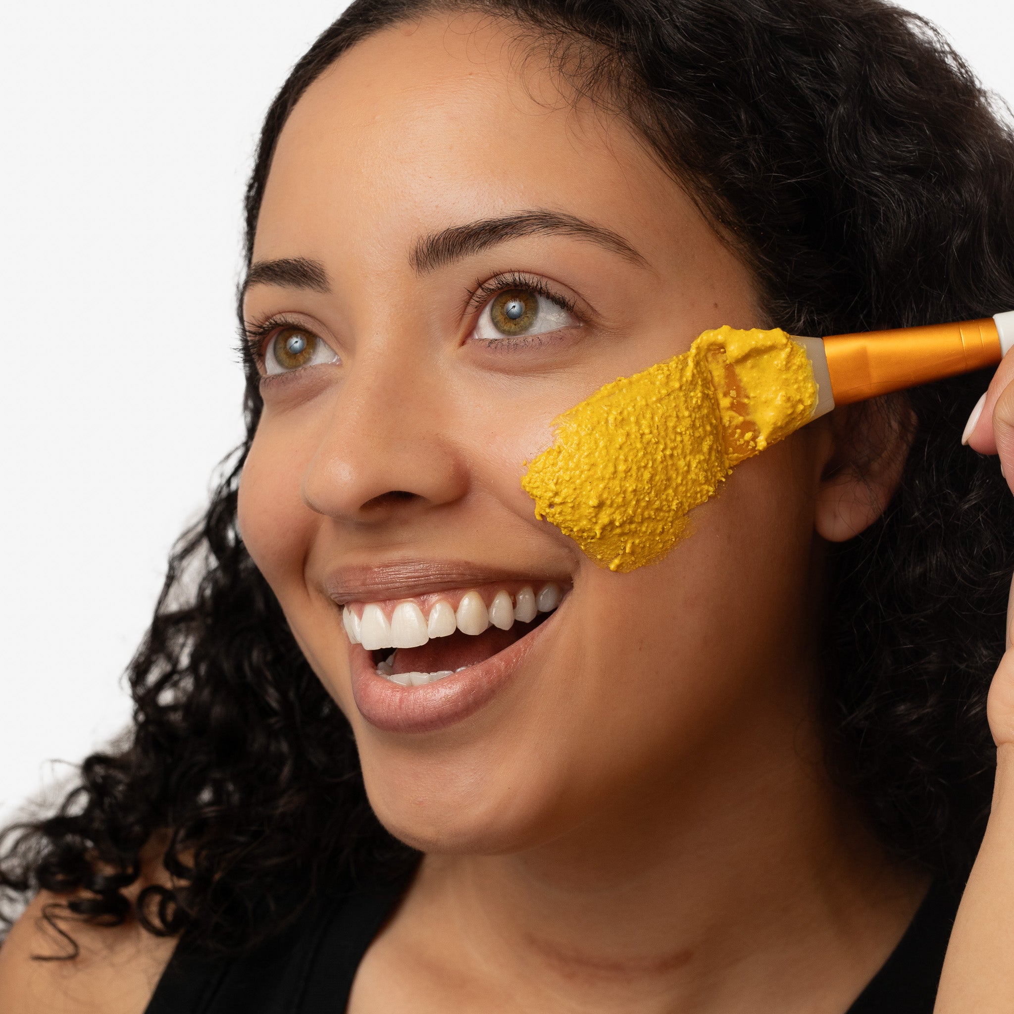 Woman having yellow turmeric mask applied to her face with a brush