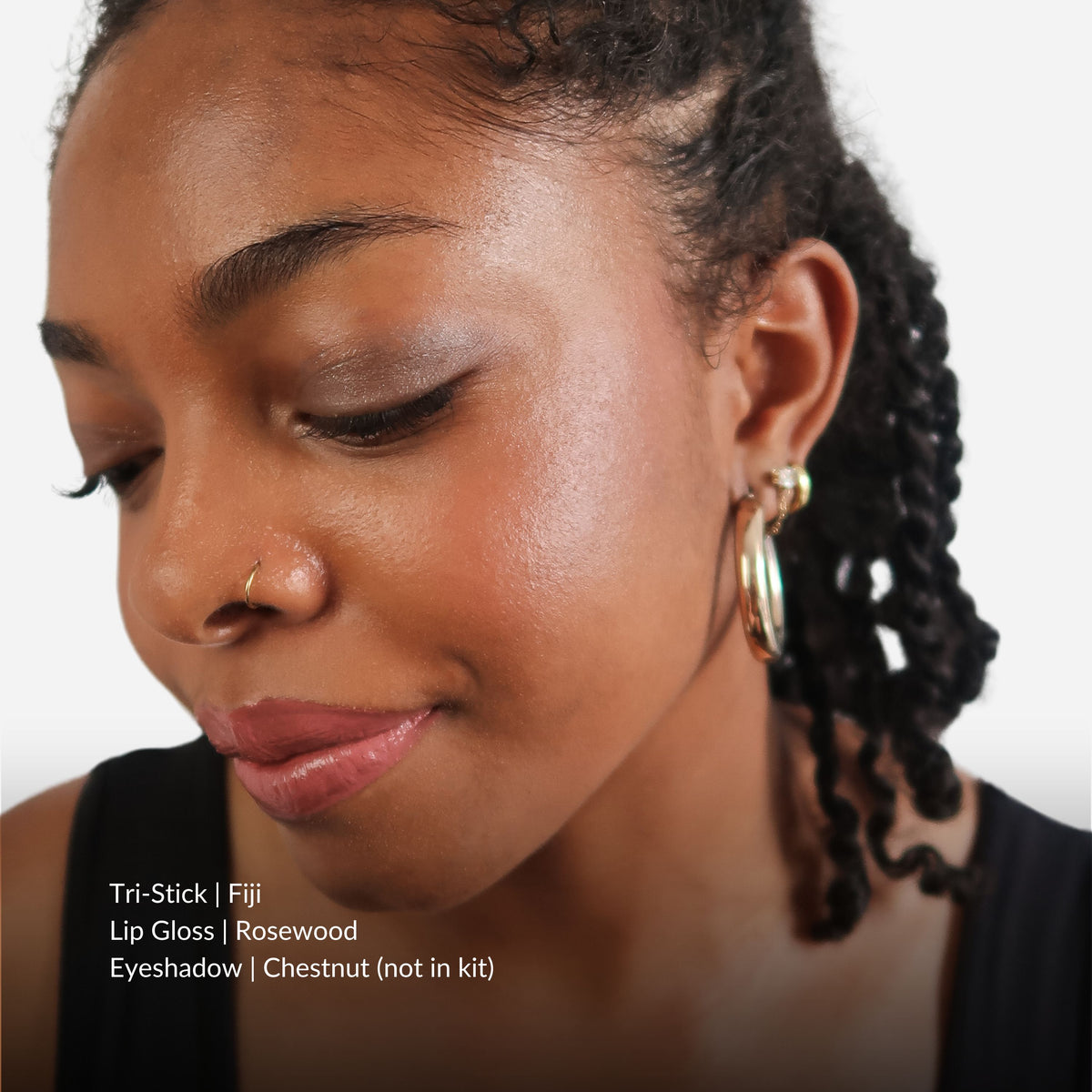 Close-up of a woman with makeup products listed on a white background. Products listed are Tri-Stick Fiji, Lip gloss Rosewood, Eyeshadow Chestnut