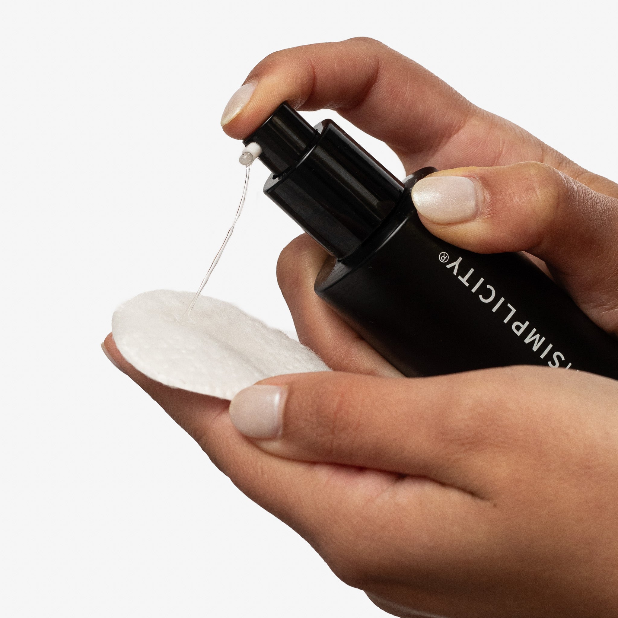 Hand holding a black withSimplicity skincare product with a dropper over a white pad on a neutral background