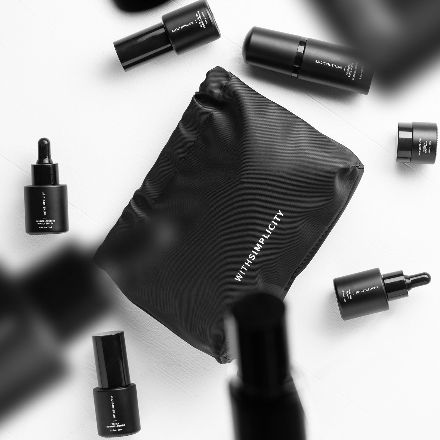 Black bottle clean skincare products falling on to a white background with a black withSimplicity makeup pouch