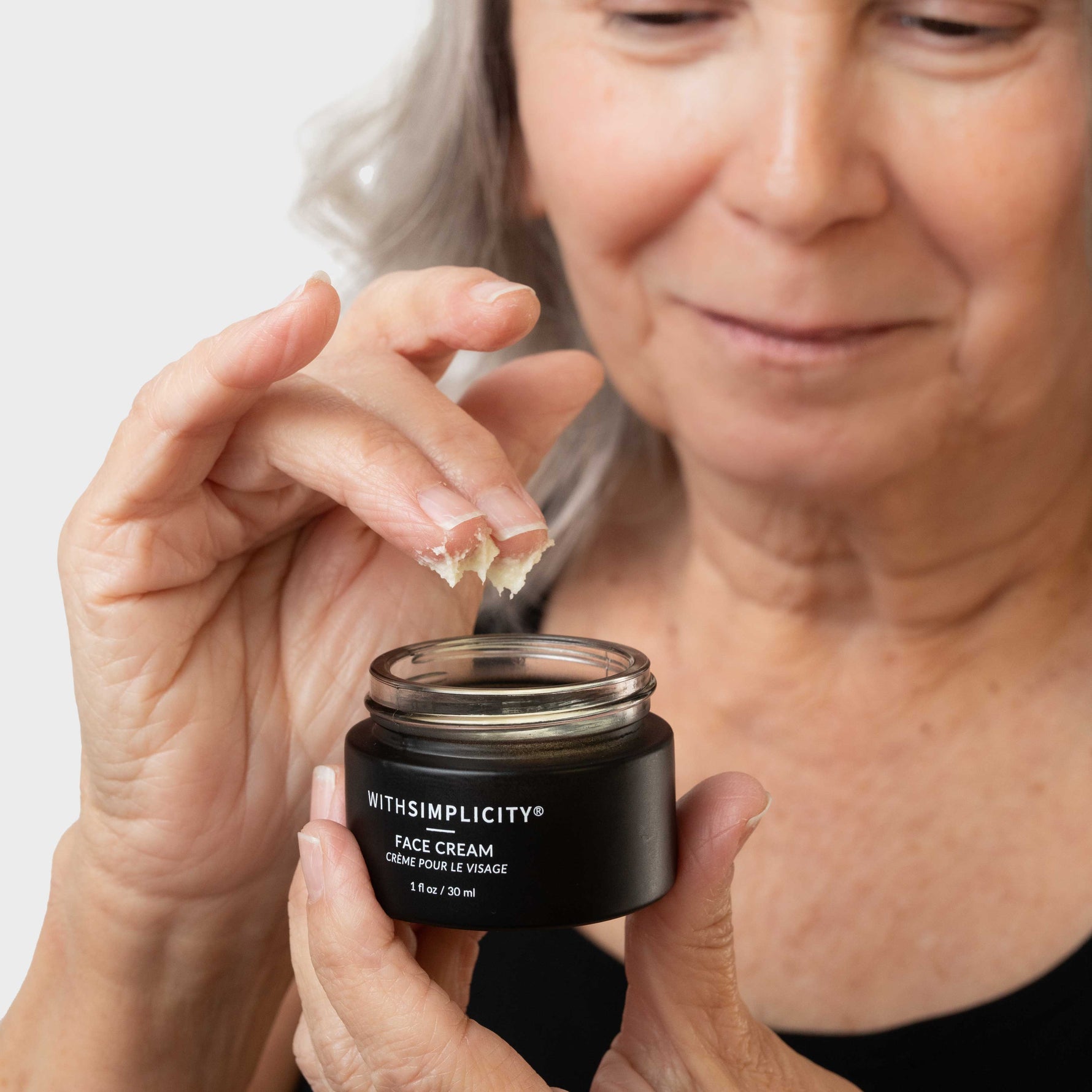 Woman holding a jar of face cream with a neutral background
