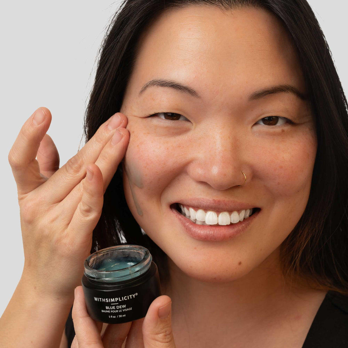 woman applying withSimplicity Blue Dew to face against light gray background