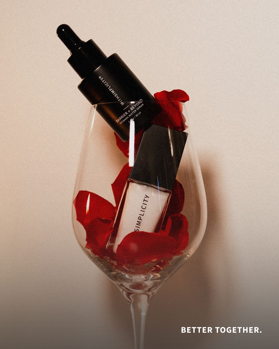 A romantic close-up of withSimplicity’s Barrier + Beyond Vitamin Water Serum and Face Primer resting inside a clear wine glass filled with red rose petals. The words “BETTER TOGETHER.” appear in white text in the bottom corner.