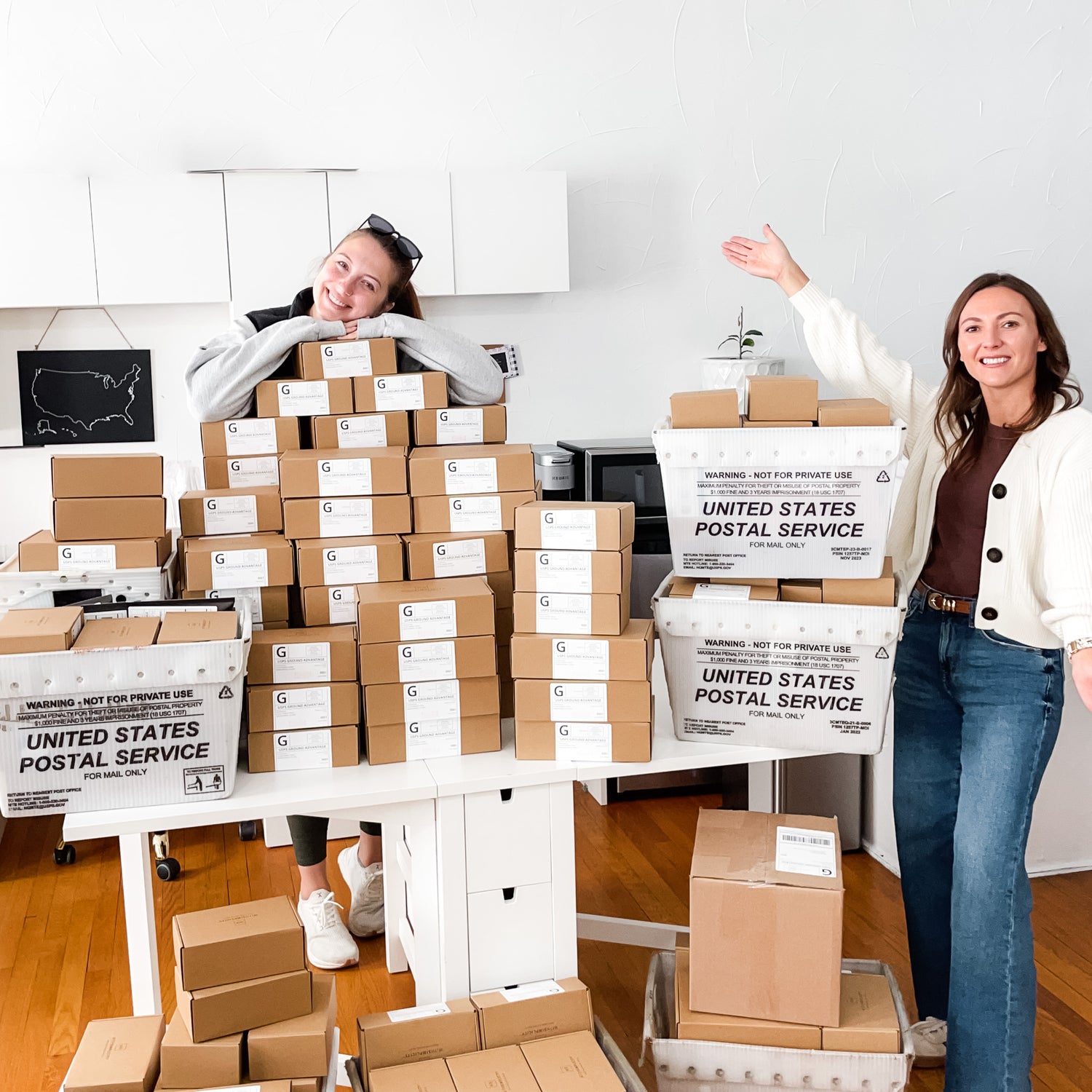 Two women standing beside stacks of withSimplicity shipping boxes and USPS boxes