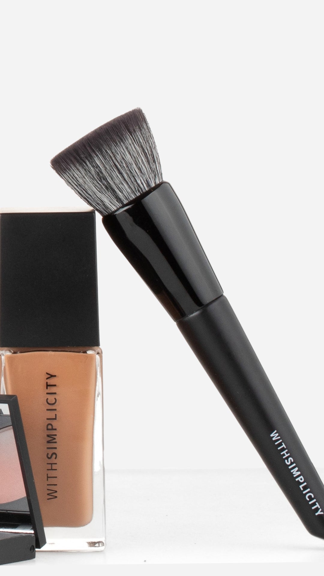 withSimplicity black foundation brush leaning against Liquid Foundation bottle against a white background