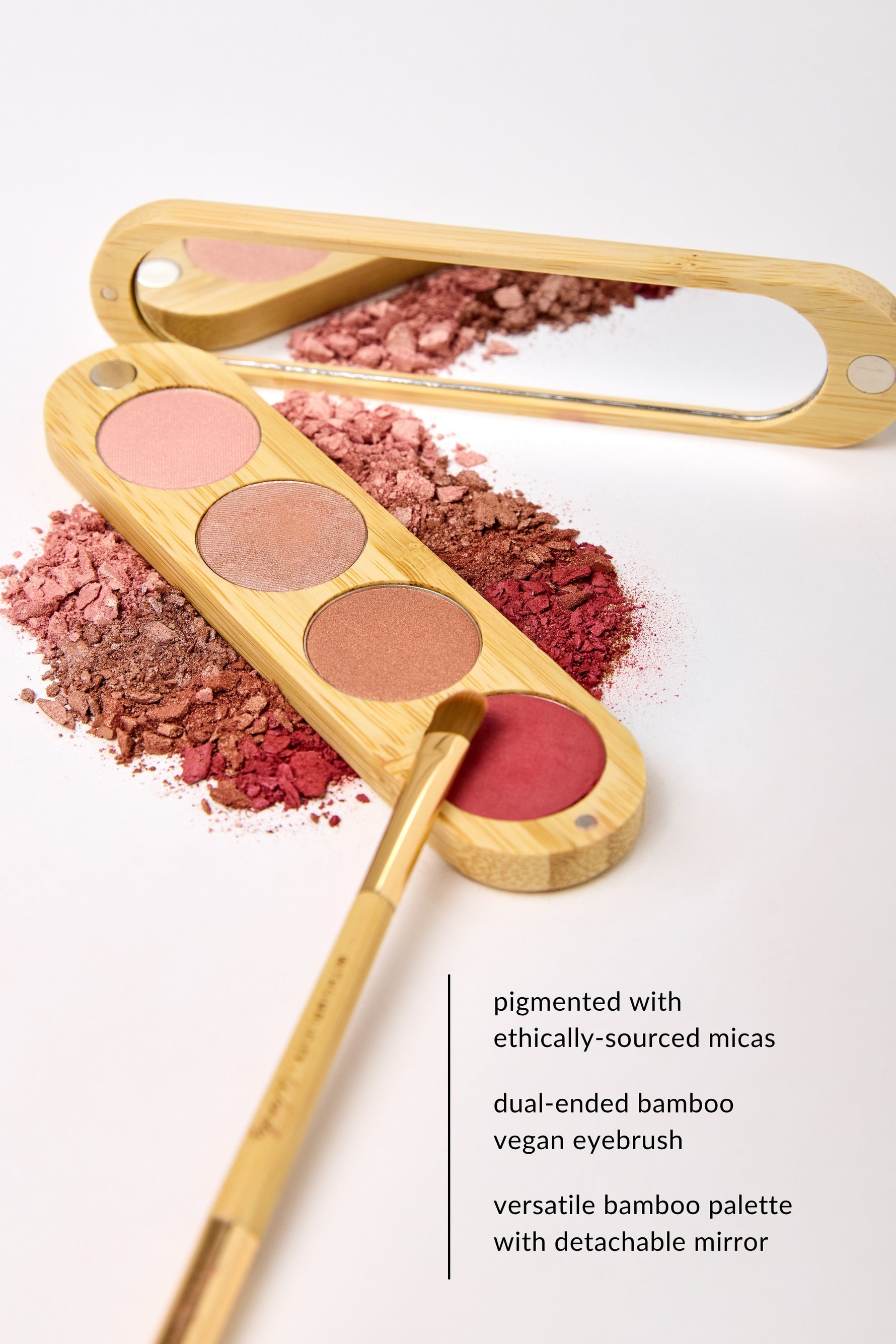 A bamboo makeup palette with four eyeshadow pans in pink, brown, and red tones, plus a matching bamboo applicator brush and a built-in mirror, styled on a white background with crushed powder behind it. Text on the right describes the product features.