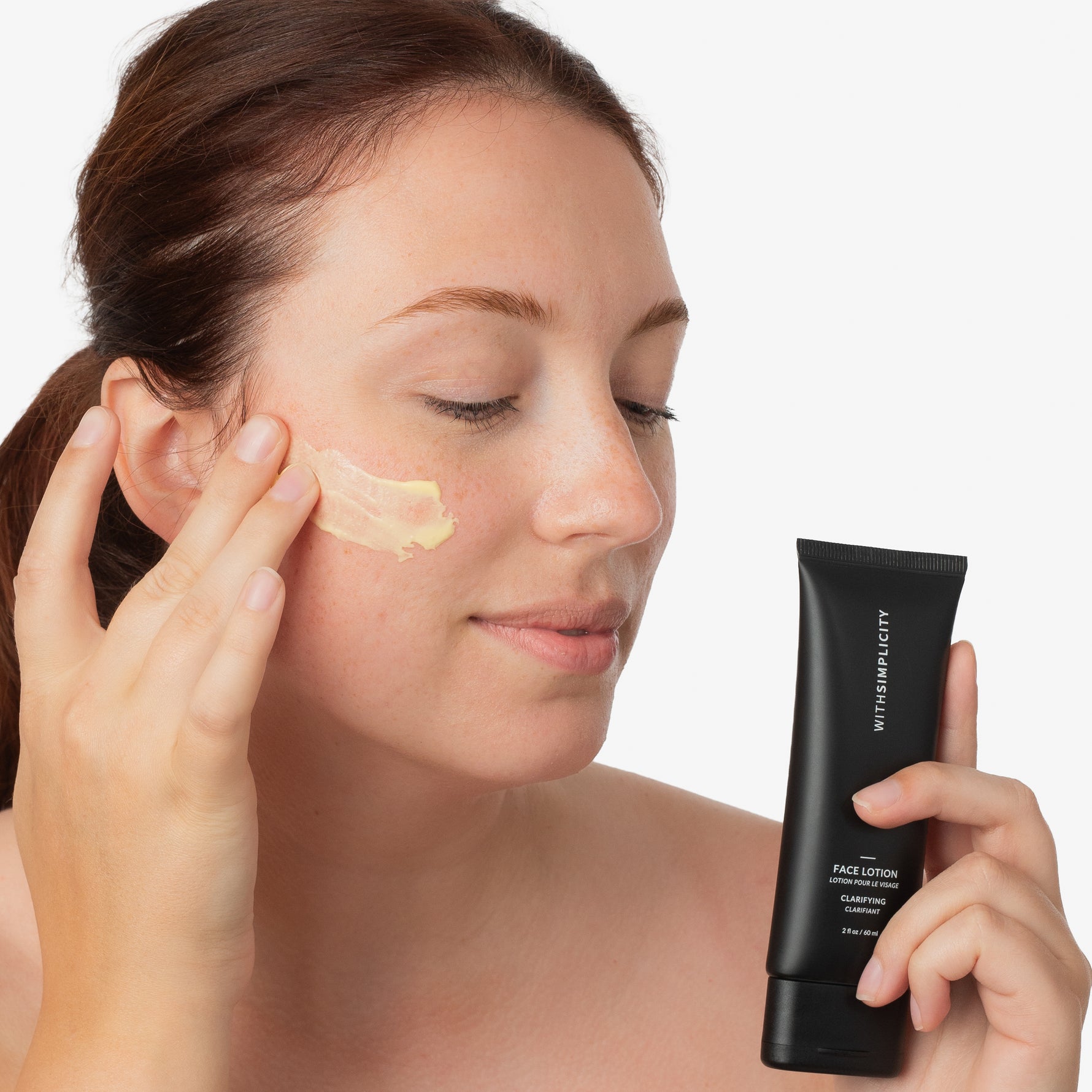 Model with reddish-brown hair applying swatch of withSimplicity Clarifying Face Lotion to face against white background