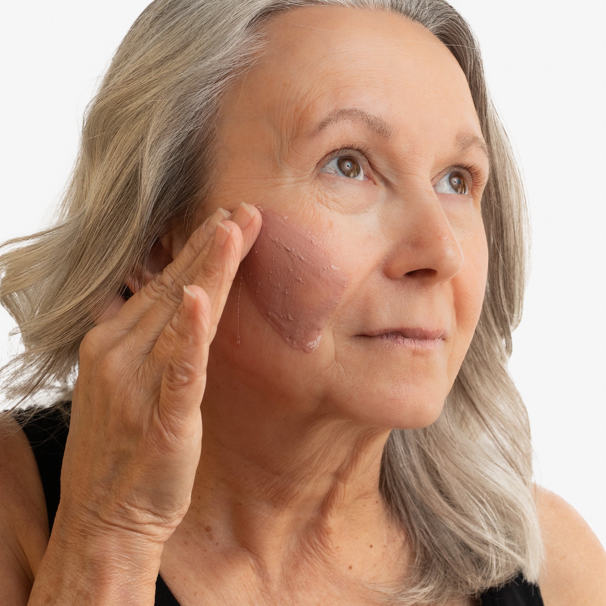 Woman applying a withSimplicity anti-aging Face Mask to her face with a white background