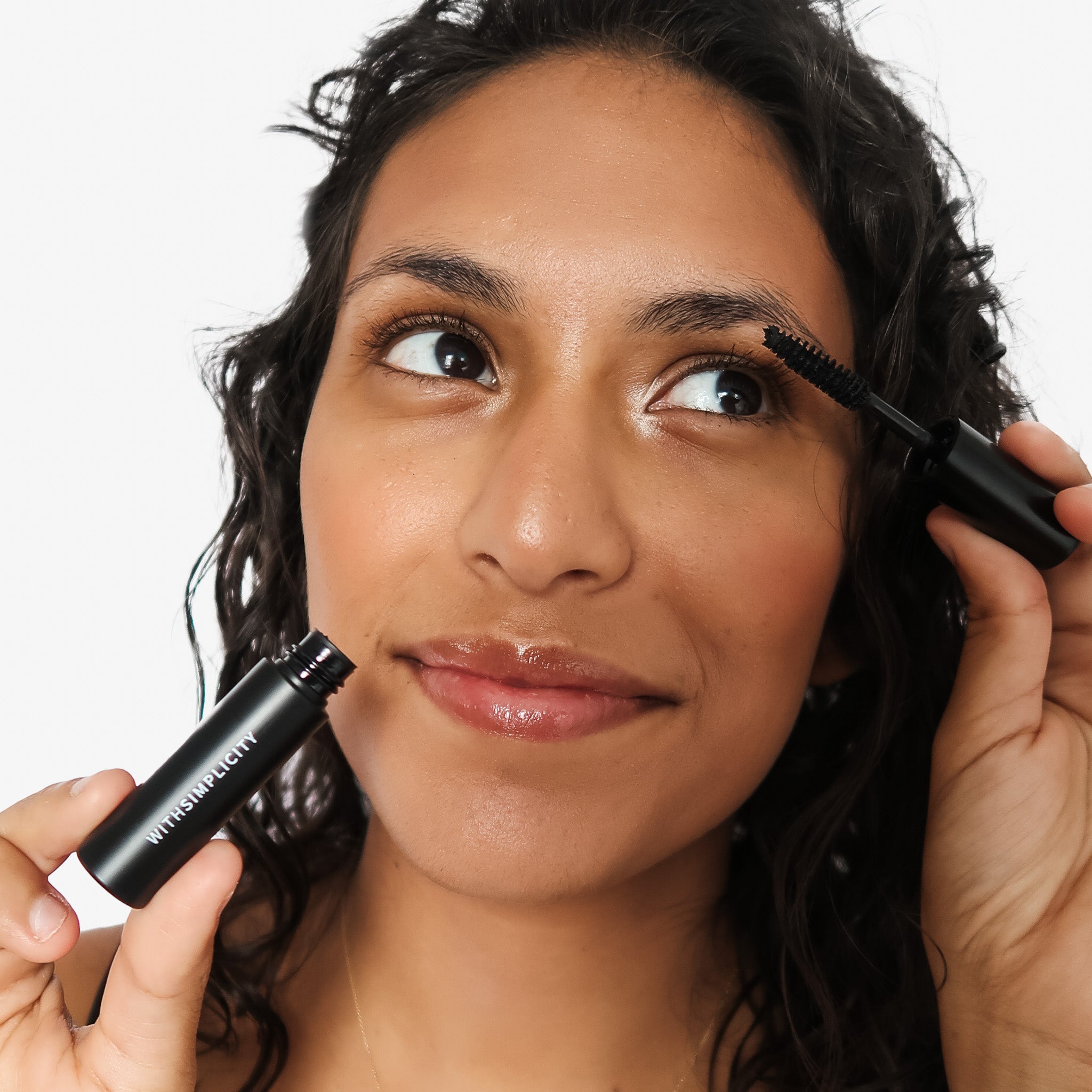 Woman applying withSimplicity clean mascara with a black mascara wand against a white background
