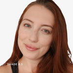 Close-up of a woman with red hair and green eyes on a white background. Text says Shade 0.5