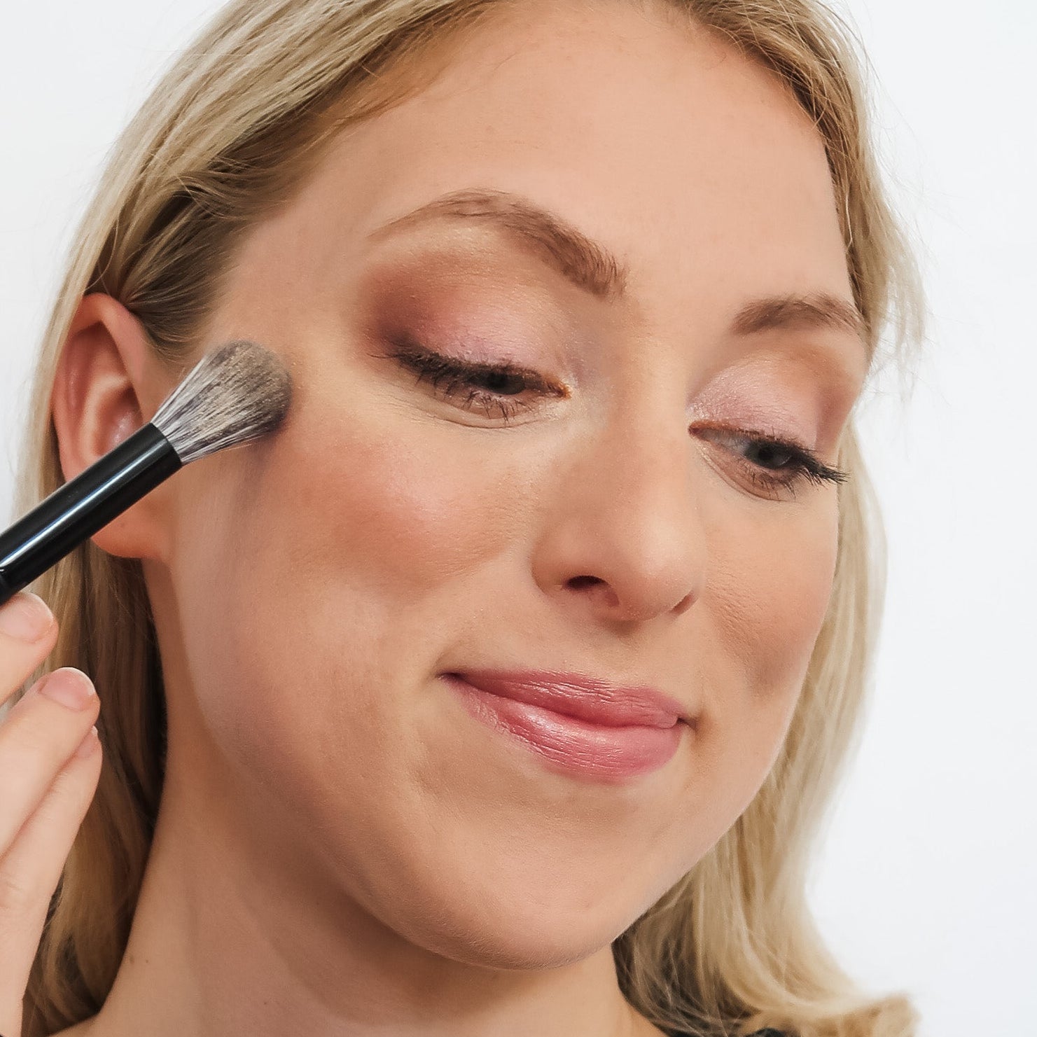 Woman applying makeup with a brush and compact powder on a white background