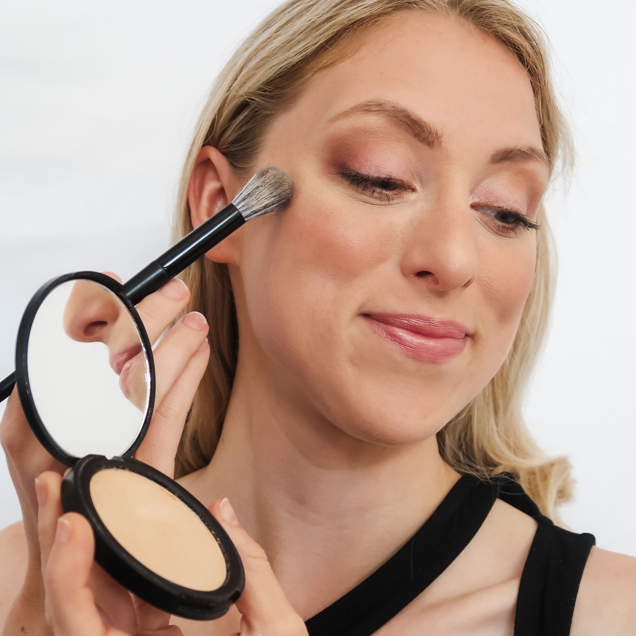 Woman applying makeup with a brush and compact powder on a white background